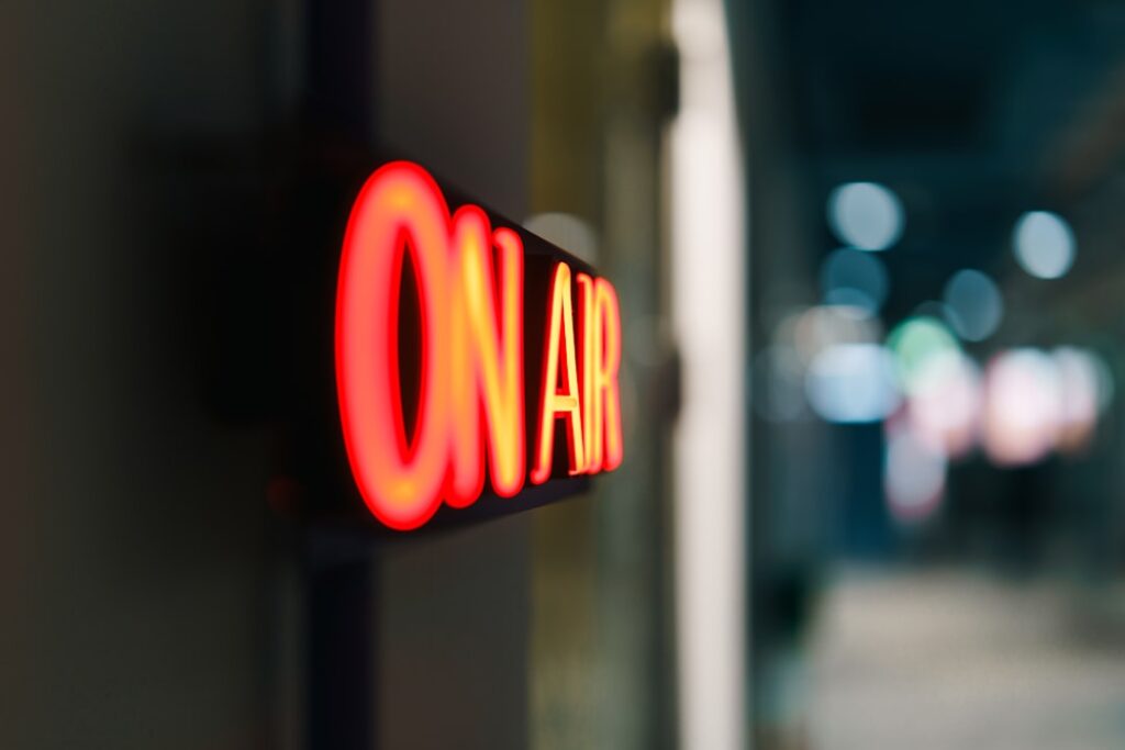 Broadcast studio air sign radio podcast streaming production illuminated in red neon light symbolizing active session